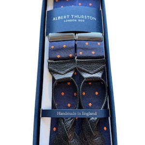 Puede incluir: Un par de tirantes azul marino con lunares naranja. Los tirantes están en una caja con el texto "Albert Thurston London 1820" y "Handmade in England".