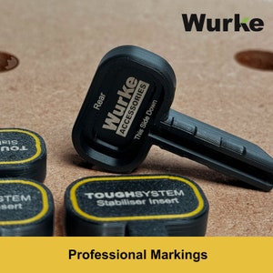 May include: Black key with the text "Wurke Accessories" and "This Side Down" on it. The key is on a brown surface with other black and yellow objects with text on them. The text on the other objects reads "TOUGHSYSTEM Stabiliser Insert" and "STEM sert".