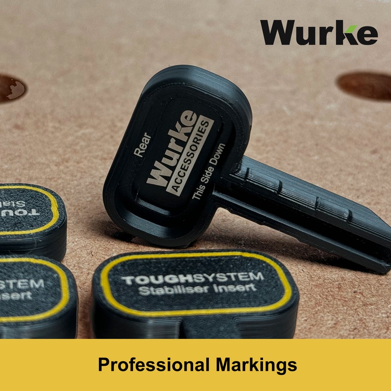 May include: Black key with the text "Wurke Accessories" and "This Side Down" on it. The key is on a brown surface with other black and yellow objects with text on them. The text on the other objects reads "TOUGHSYSTEM Stabiliser Insert" and "STEM sert".