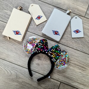 May include: Two passport holders in cream and light grey, each with a matching luggage tag featuring a red Mickey Mouse icon over blue waves. A black headband with a sequined bow and clear ears filled with colourful star-shaped confetti.