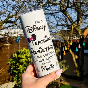 May include: White stainless steel tumbler with a black and pink design. The tumbler features the text "I'm a Disney Teaching Assistant. It's like a regular teaching assistant but with magic."