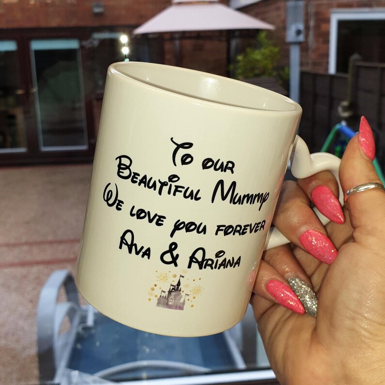 May include: White ceramic mug with black text that reads "To our Beautiful Mummy We love you forever Ava & Ariana". The mug has a gold glitter image of a castle with fireworks.