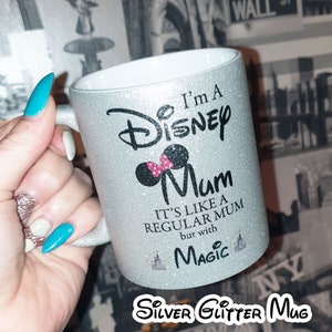 May include: A silver glitter mug with a black and white graphic that says "I'm a Disney Mum. It's like a regular mum but with magic." The graphic also includes a black silhouette of Mickey Mouse's head with a pink bow.