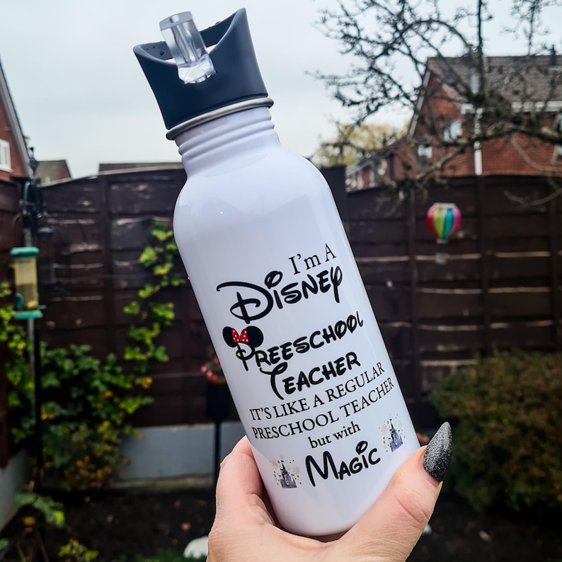 May include: White water bottle with a black lid and a straw. The bottle has a black and white design with the text "I'm a Disney Preschool Teacher. It's like a regular preschool teacher but with Magic."