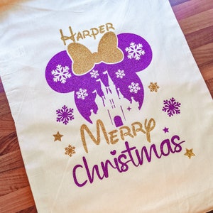 May include: A white canvas tote bag with a purple and gold glitter design. The design features Mickey Mouse ears with a bow, a castle, snowflakes, and the text "Harper Merry Christmas".