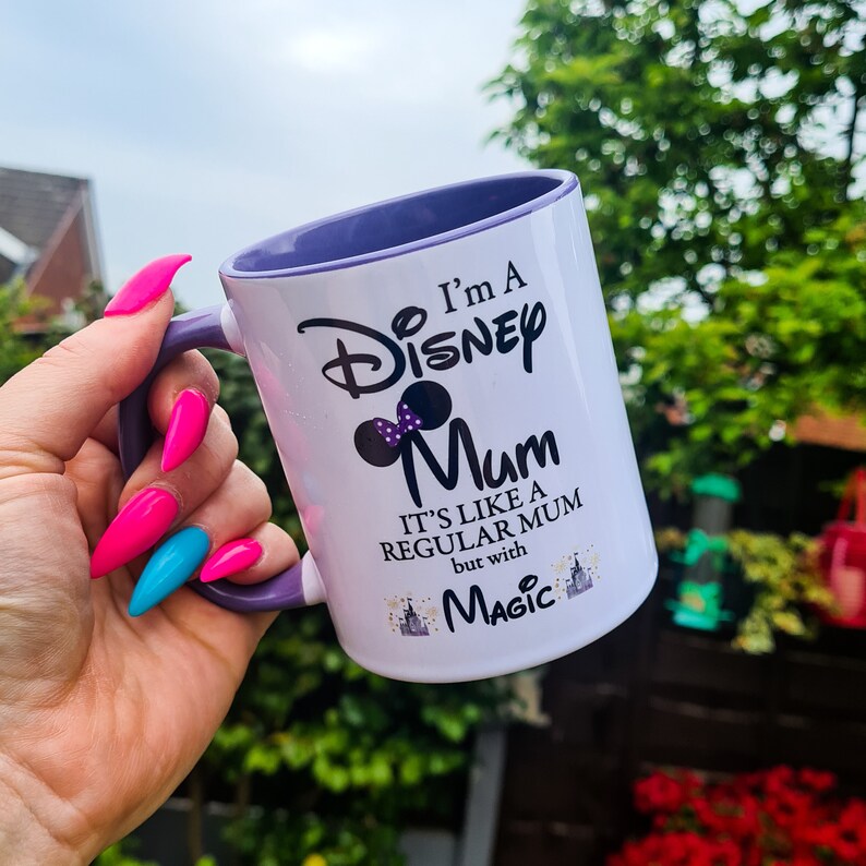 May include: White ceramic mug with a purple rim. The mug has a black and purple design that says "I'm a Disney Mum. It's like a regular mum but with magic."
