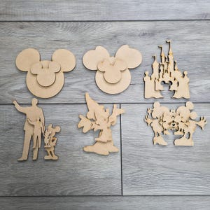 May include: A selection of unfinished wooden cutouts depicting cartoon characters and symbols. Includes Mickey Mouse head shapes, a castle, a wizard, and a family silhouette with Mickey Mouse.