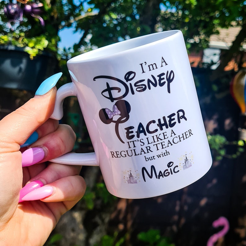 May include: White ceramic mug with a black design that says "I'm a Disney Teacher. It's like a regular teacher but with magic." The design also includes a black silhouette of Mickey Mouse's head with a pink bow.