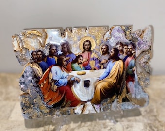 May include: A framed painting depicting the Last Supper, featuring Jesus and his disciples gathered around a table. The painting is set against a gold and white background with a textured, irregular frame.