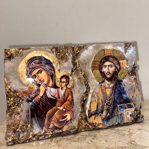 May include: A wooden plaque with a gold background and two religious icons. The left icon depicts the Virgin Mary holding a baby Jesus. The right icon depicts Jesus Christ with a halo and a cross behind him.