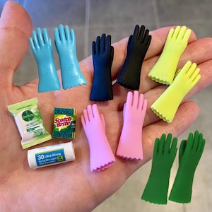 May include: A collection of miniature cleaning items. Includes blue, black, yellow, pink, and green rubber gloves, a green and white packet, a green and yellow sponge, and a roll of white bin liners.