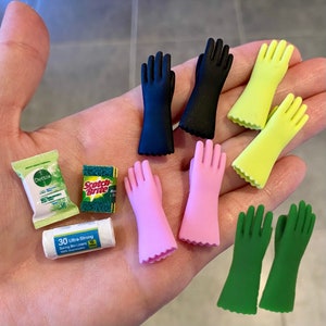 Può includere: Una mano che tiene una varietà di prodotti per la pulizia, tra cui guanti per lavare i piatti verdi e gialli, guanti da forno rosa, guanti per lavare i piatti neri, una spugna verde, una spugna abrasiva verde e bianca e una scatola bianca di sacchetti per la spazzatura. La scatola di sacchetti per la spazzatura dice "30 Ultra Strong Swing Bin Liners 100% Biodegradable".