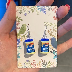 Może przedstawiać: Zestaw trzech ceramicznych kubków z nakrapianą, kremową glazurą. Każdy kubek zdobi ręcznie malowany kwiatowy wzór w odcieniach niebieskiego, zielonego i żółtego. Kubki mają prosty, zaokrąglony kształt i wygodny uchwyt.