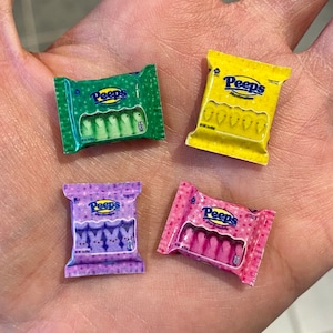 May include: Four miniature boxes of Peeps marshmallow candies. The boxes are yellow, green, pink, and purple. Each box has a different flavor of Peeps: yellow, green, pink, and purple.