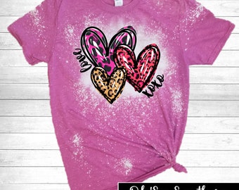 May include: A pink t-shirt with a bleached design featuring three hearts with animal print patterns. The words "Love" and "XOXO" are written on the shirt. The bottom right corner of the shirt has the text "Oh'So Southern Boutique".