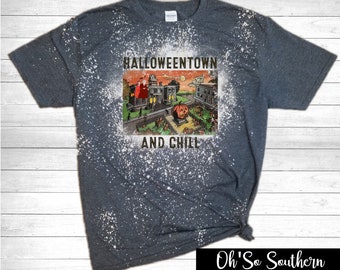 May include: Dark gray t-shirt with a distressed, bleached effect. The shirt features a vintage-style graphic of a Halloween town scene with a jack-o'-lantern and the text "Halloweentown and Chill". The bottom right corner has the text "Oh'So Southern Boutique".