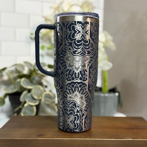 Puede incluir: Un vaso t&eacute;rmico azul marino con un dise&ntilde;o de mandala floral plateado y las palabras "FUCK OFF" repetidas alrededor del dise&ntilde;o. El vaso tiene un asa y una tapa azul oscuro. El vaso est&aacute; sobre un soporte de madera.