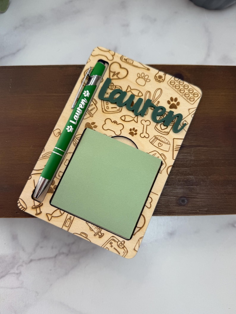 May include: A wooden notepad holder with a green notepad and a green pen. The holder is engraved with pet-themed icons and the name "Lauren" in green. The pen has the name "Lauren" printed on it.
