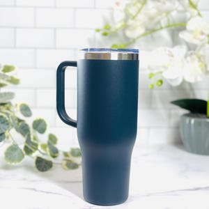 Puede incluir: Un vaso t&eacute;rmico azul marino con asa y tapa transparente. El borde y el asa de acero inoxidable contrastan con el acabado mate. Dise&ntilde;ado para mantener las bebidas calientes o fr&iacute;as.