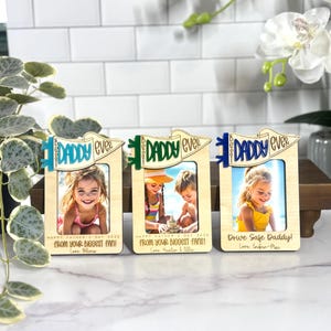 May include: Three wooden photo frames with the words "Best Daddy Ever" in blue, green, and blue. Each frame holds a photograph and includes text that reads "Happy Father's Day 2023" and "From your biggest fan!"