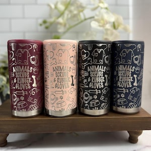 Puede incluir: Cuatro vasos de acero inoxidable en borgoña, melocotón, negro y azul marino. Cada vaso presenta un diseño plateado con ilustraciones médicas y el texto "ANIMALS SCRUBS & RUBBER GLOVES".