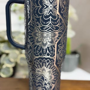 Puede incluir: Un vaso t&eacute;rmico azul marino con un dise&ntilde;o de mandala plateado y las frases "Fuck Off", "Fuck It" y "What the Fuck?" impresas. El vaso tiene un asa azul oscuro y una tapa transparente.
