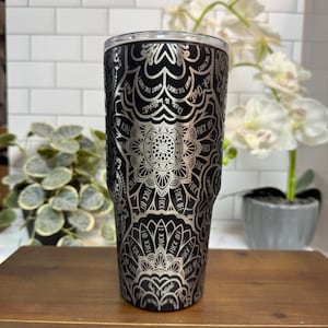 Puede incluir: Vaso negro y plateado con un dise&ntilde;o de mandala y las palabras "FUCK OFF" y "What the fuck?" repetidas. El vaso tiene una tapa plateada y est&aacute; sobre una superficie de madera.