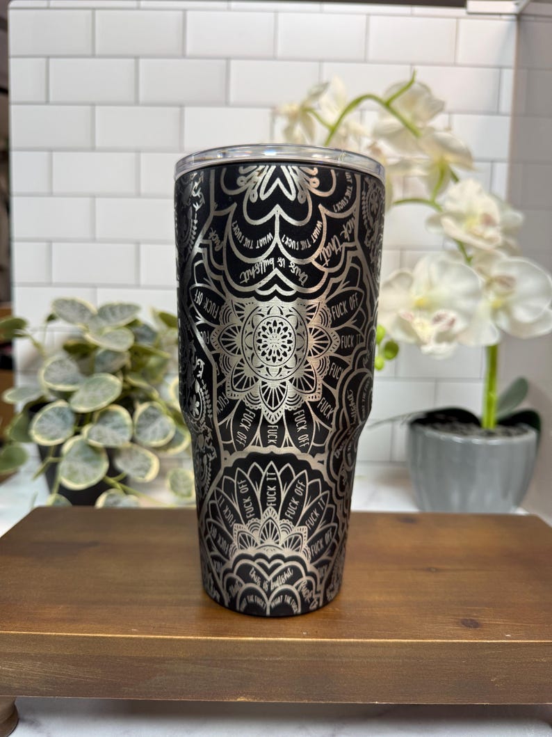 Puede incluir: Vaso negro y plateado con un dise&ntilde;o de mandala y las palabras "FUCK OFF" y "What the fuck?" repetidas. El vaso tiene una tapa plateada y est&aacute; sobre una superficie de madera.