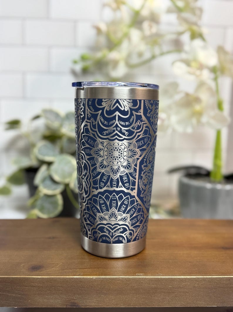 Puede incluir: Un vaso de acero inoxidable azul marino con un dise&ntilde;o de mandala plateado. El dise&ntilde;o incluye las palabras "FUCK OFF" y "this is bullshit". El vaso tiene un borde plateado y una tapa transparente.
