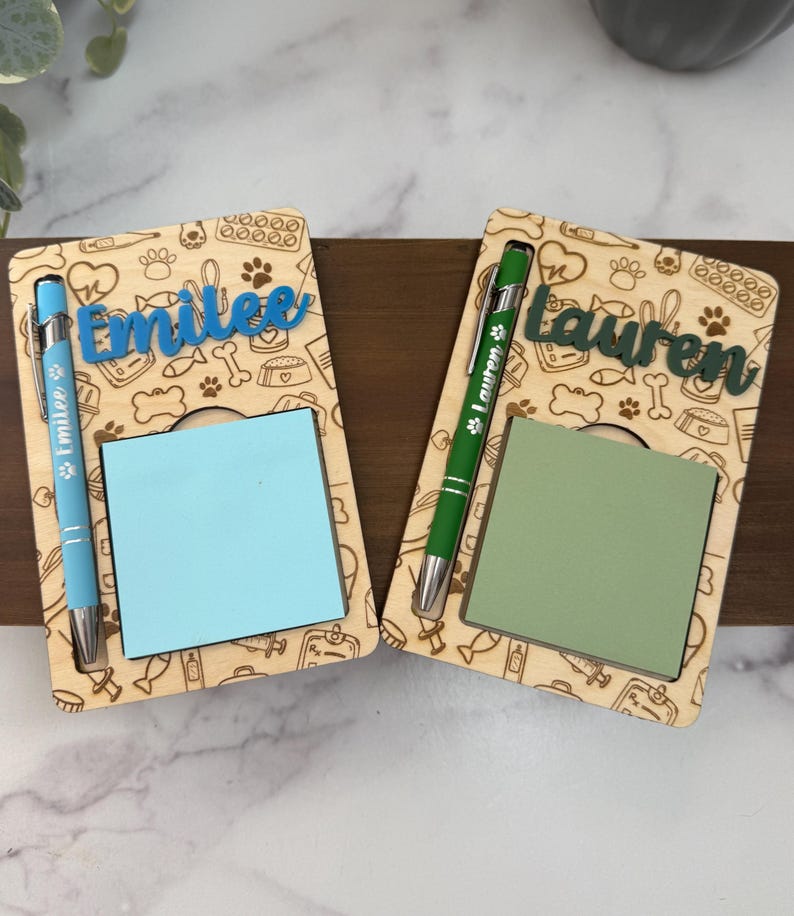 May include: Two wooden desk organizers with a pet-themed design. Each has a name cut-out, a notepad, and a pen. One has "Emilee" in blue, the other has "Lauren" in green. The pens are blue and green.