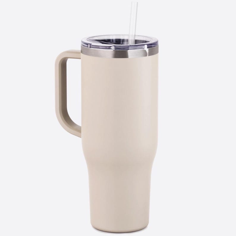 Puede incluir: Un vaso t&eacute;rmico de color crema con asa y pajita transparente. El vaso tiene un borde plateado y una tapa transparente. El asa es del mismo color crema que el vaso. Dise&ntilde;ado para bebidas fr&iacute;as o calientes.
