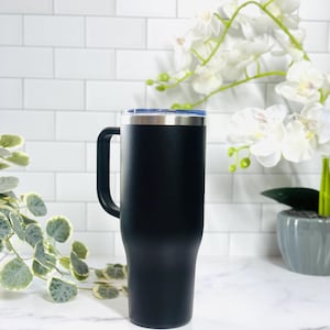 Puede incluir: Un termo de viaje negro con asa y borde plateado. El termo tiene una tapa azul y est&aacute; dise&ntilde;ado para mantener las bebidas calientes o fr&iacute;as. El termo es alto y cil&iacute;ndrico, adecuado para diversas bebidas.