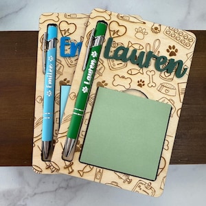 May include: Two wooden desk organizers with pens and notepads. One has a blue pen with the name "Emilee" and the other has a green pen with the name "Lauren". Both organizers have a pet-themed design and a green notepad.
