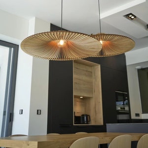 May include: Two large, round, wooden pendant lights with a woven, fan-like design hang over a dining table. The lights are illuminated with warm, white light bulbs.