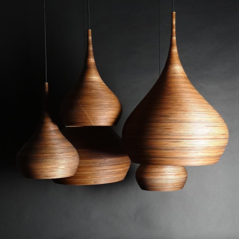 May include: Four wooden pendant lights in a teardrop shape, hanging from the ceiling. The lights are made of thin strips of wood, creating a layered effect. The lights are all different sizes, with the largest one at the top and the smallest one at the bottom.