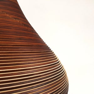 May include: A close-up of a wooden lampshade made of thin, stacked, concentric rings of wood. The rings are a dark brown color and create a smooth, rounded shape.