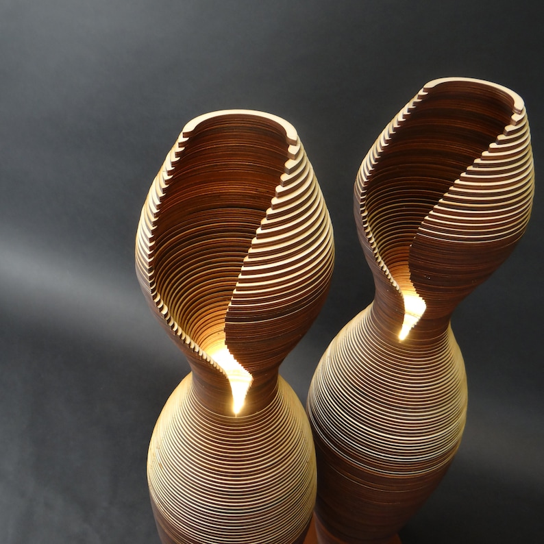 May include: Two wooden lamps with a unique, layered design. The lamps are lit and have a warm, inviting glow.