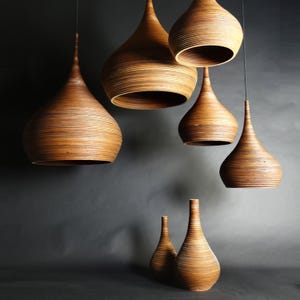 May include: A set of six wooden pendant lights in various sizes, all with a teardrop shape and a natural wood finish. The lights are hanging from black cords against a dark background.