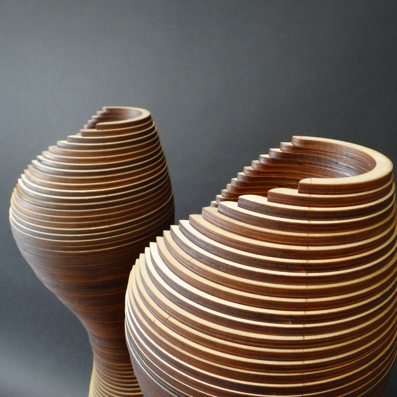 May include: Two wooden vases with a layered, spiral design. The vases are made of thin strips of wood that are stacked on top of each other to create a unique and modern look.