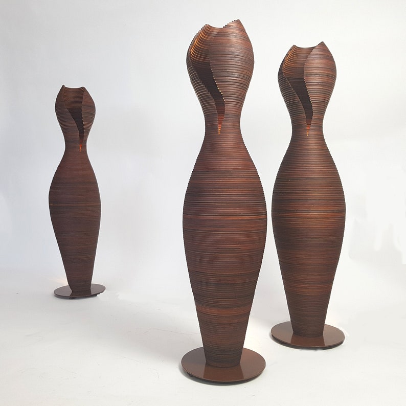 May include: Three tall, brown, wooden floor lamps with a unique, organic, wavy design. The lamps are lit and cast a warm glow.