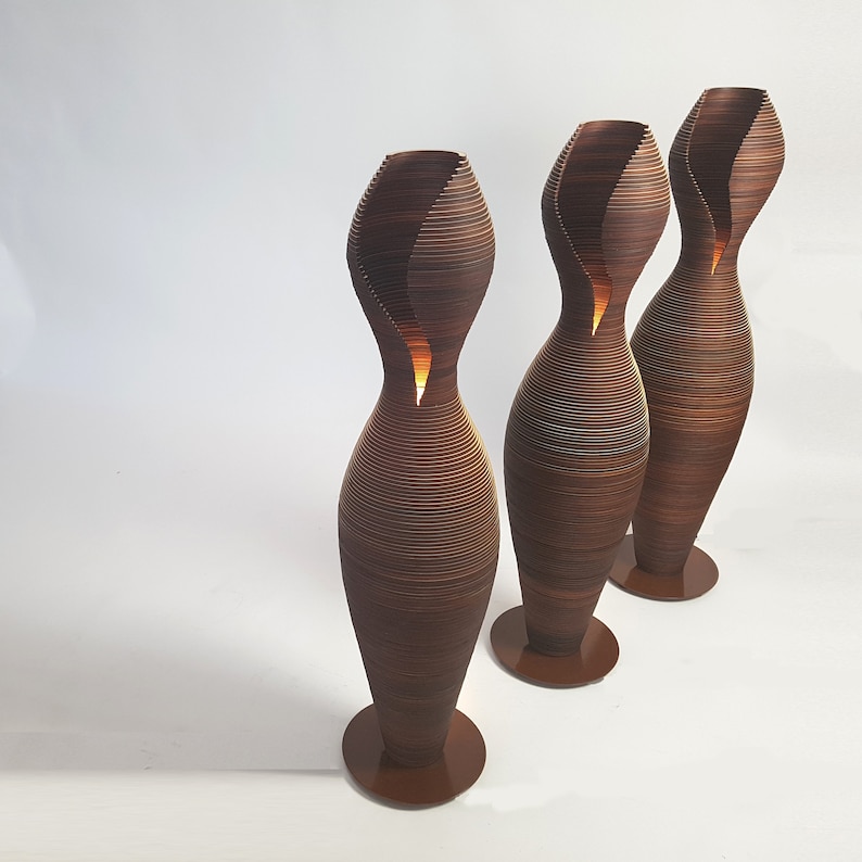 May include: Three brown, wooden, floor lamps with a unique, wavy, organic design. The lamps are lit and have a warm glow.