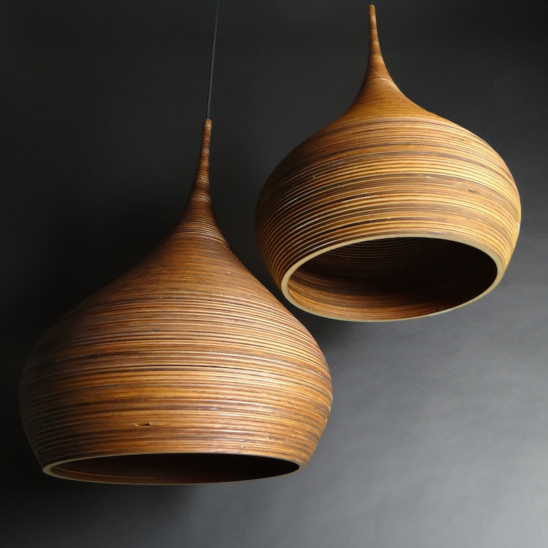 May include: Two brown, woven, pendant light fixtures with a teardrop shape hang from the ceiling against a dark gray background.