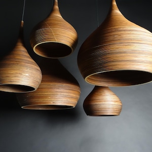 May include: Five wooden pendant lights with a teardrop shape and a layered design. The lights are hanging from the ceiling and are all turned off.
