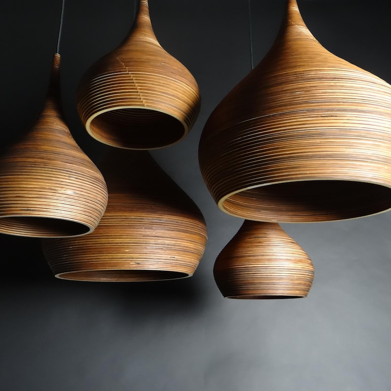 May include: Five wooden pendant lights with a teardrop shape and a layered design. The lights are hanging from the ceiling and are all turned off.