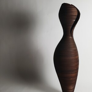 May include: A tall, dark brown vase made of thin, stacked wooden slats. The vase has a unique, organic shape with a narrow neck and a wide base.