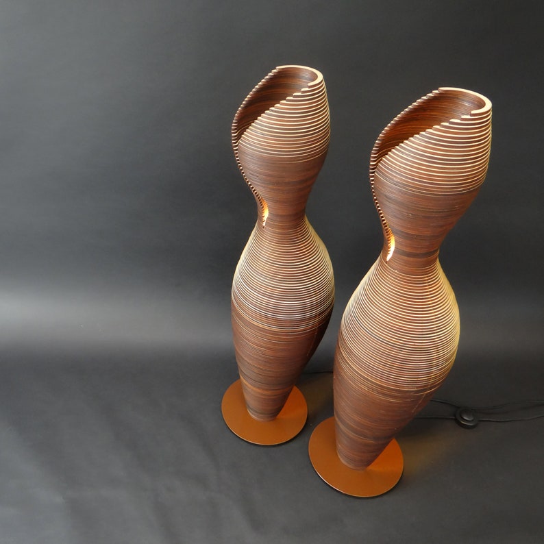 May include: Two tall, brown, wooden floor lamps with a unique, layered, spiral design. The lamps have a warm, ambient glow.