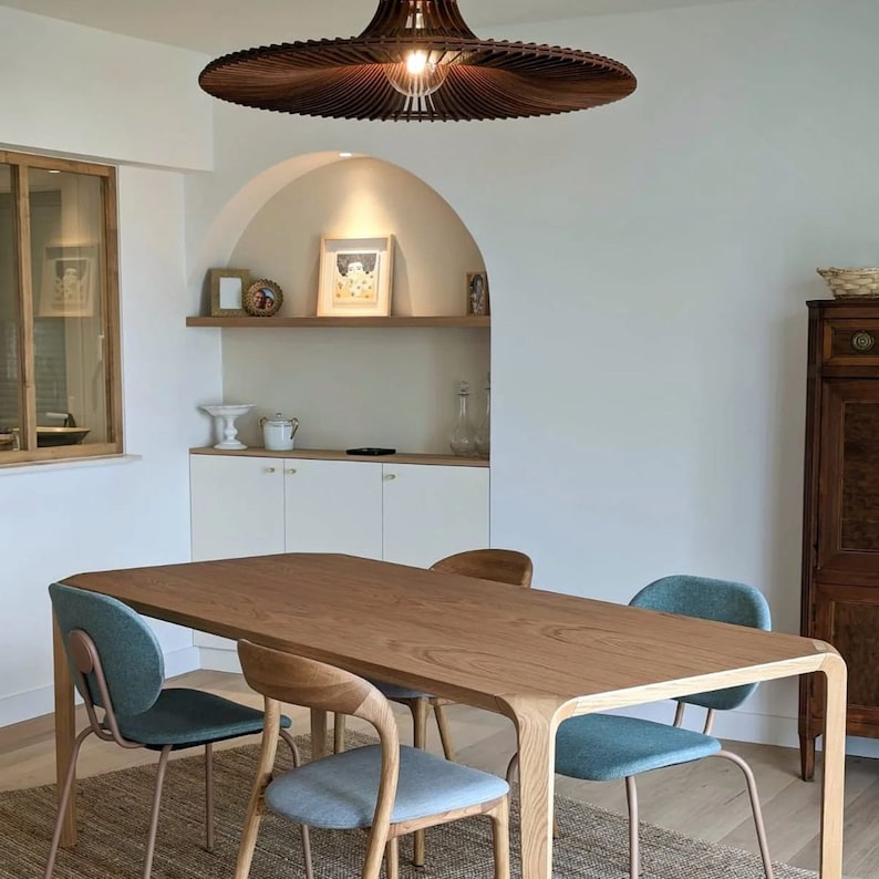 May include: A wooden dining table with a light brown finish and a curved edge. The table is surrounded by four teal blue chairs with metal legs. A large, brown, fan-shaped light fixture hangs above the table.