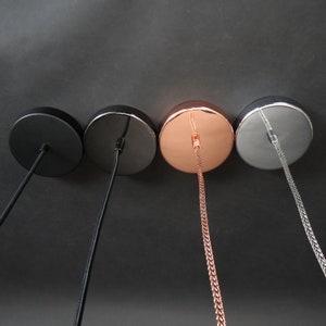 May include: Four ceiling light fixture canopy covers in different finishes: black, silver, copper, and chrome. Each canopy has a cord hanging from it.
