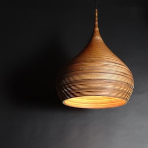 May include: A wooden pendant light with a teardrop shape and a warm, natural wood finish. The light is made of thin strips of wood that are layered together to create a unique and textured look.