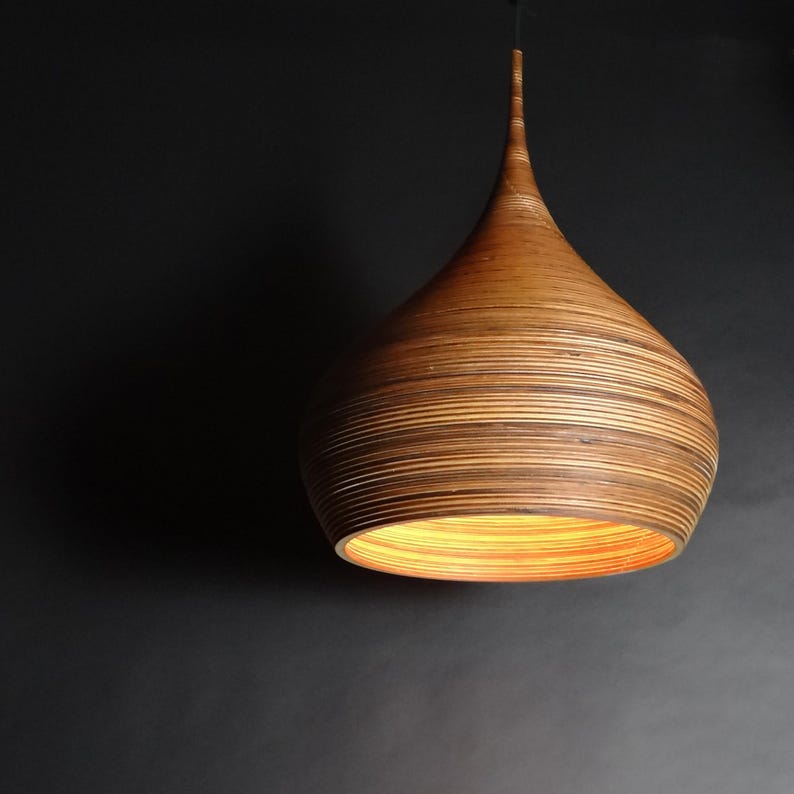 May include: A wooden pendant light with a teardrop shape and a warm, natural wood finish. The light is made of thin strips of wood that are layered together to create a unique and textured look.